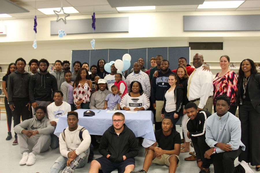 Palmettos football family and administration join senior Kenneth Spiller at the table where he chose to play football for Charleston Southern University.​